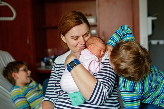 Mother holding newborn baby girl in hospital bed, with two sons sitting beside her. Real life, real people moment of family love, siblings bonding, and joy of welcoming a new child.