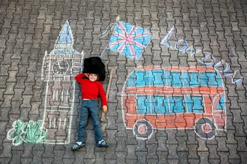 Fototapete Londoner Roter Bus Happy little boy in Queens Guard uniform drawing London-themed chalk art with Big Ben, red bus, and Union Jack. Real life, real people moment of creative outdoor play and British imagination.  © Irina Schmidt