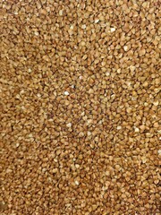 a close-up, top-down view of a dense, even layer of roasted buckwheat groats. The groats are small, triangular, and have a rich, warm brown and tan color palette, providing a uniform texture ideal for
