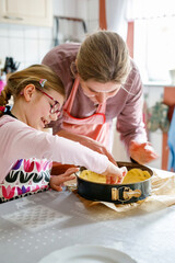 Little cute girl helps her mother bake a cake in the kitchen. Child and woman mixing ingredients...