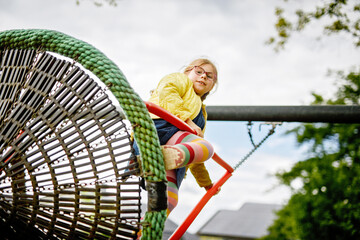 Little school girl swinging on big chain swing on school yard. Happy child enjoying school break