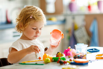 Adorable cute little toddler girl with colorful clay at home. Healthy baby playing and creating toys from play dough at nursery or playschool. Small kid molding modeling clay, creative activity