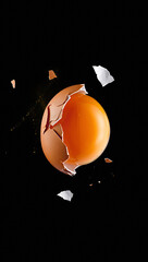 Obraz premium A cracked egg with a bright yellow yolk against a stark black background with shell fragments