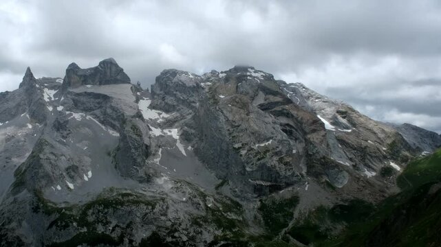 Majestic alpine mountains with rugged rock faces and patches of snow rise under overcast skies, revealing nature&rsquo;s raw power and dramatic beauty in high elevation.
