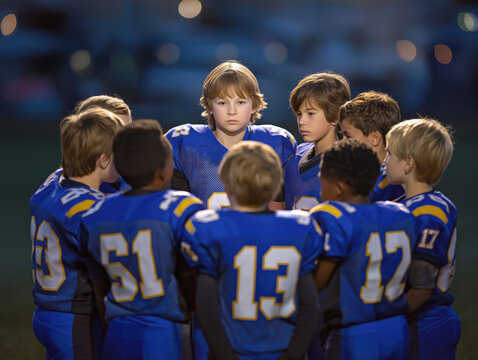 Group of young male athletes in blue football uniforms huddled together on the field, focused on strategy and teamwork during a game, showcasing camaraderie and determination