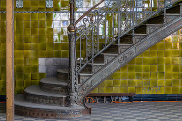 Historic decorative cast iron staircase leading upward, set against a wall covered with green...