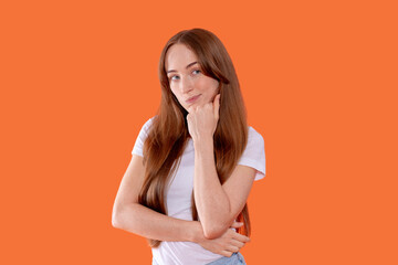 Young woman with long hair poses thoughtfully against an orange background while wearing a casual...
