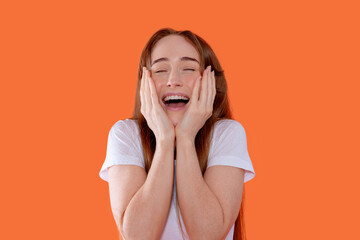 Young woman expresses joy and excitement against a bright orange background, showcasing emotions of...