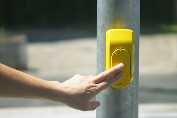 Close-up of man’s hand interacting with street technology by pressing pedestrian crossing button. Concept of responsive infrastructure, smart cities and everyday communication with automated systems