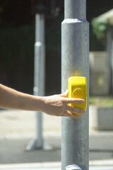 An immersive look at the use of infrastructure technologies on urban streets: hand pushing yellow crosswalk button. Concept of accessible cities and public interaction with assistive traffic systems