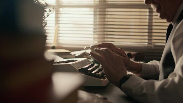 Side view shot of inspired elderly Caucasian male writer working on new bestseller on vintage typewriter in dimly lit study