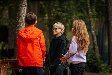  Three children talk outdoors in a wooded area one wearing an orange jacket, one in black with...