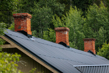 A rustic wooden house with a tin roof and red chimneys is partially hidden behind lush green...