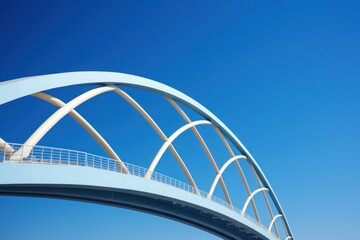 Obraz premium Modern light blue and white pedestrian bridge arching against a clear blue sky, representing infrastructure, engineering, and connection