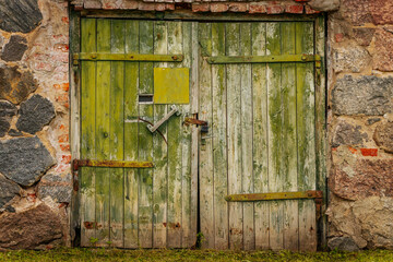 Old green double wooden doors set in a stone wall, weathered with rusted metal details, flaking paint, and a handmade patchwork repair.
