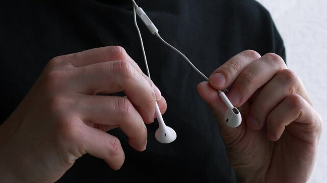 A man holds headphones in his hands to listen to music.
Music on headphones.
White wired headphones with unwound cable