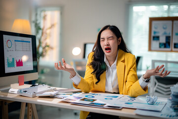 Young frustrated businesswoman screaming at her desk while looking at declining charts on her...