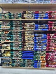 Shelves filled with neatly folded, colorful prayer rugs in a retail store, showcasing a variety of patterns and textures for religious practices.