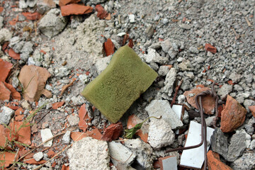 A worn green sponge lies atop shattered bricks, concrete, and metal fragments, illustrating urban...