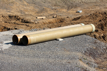 Two large beige fiberglass pipes rest on gravel in an active earthwork zone, illustrating the scale...