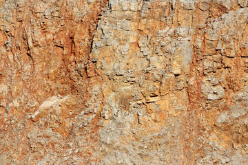 Steep rocky cliff face displays distinct layers of orange and gray stone with rugged natural...