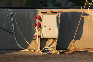 A weathered outdoor electrical cabinet with red industrial power sockets and tangled cables stands...