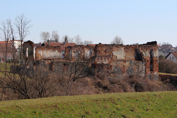 A dilapidated brick structure with exposed stone foundation stands abandoned among leafless trees...