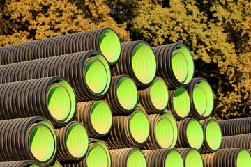 Rows of black corrugated plastic pipes with vivid green interiors are neatly stacked outdoors,...