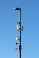 A tall streetlight pole is equipped with security cameras, antennas, and wireless transmitters,...