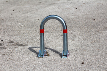 A shiny steel parking barrier with red reflective stripes and a padlock is secured to gray...