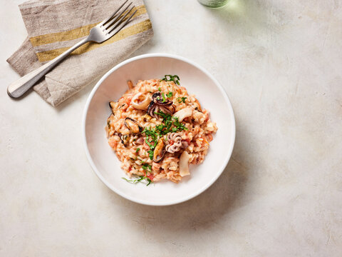 Creamy seafood risotto is artfully presented in a white bowl, showcasing shrimp and squid surrounded by fragrant herbs, perfect for a comforting meal