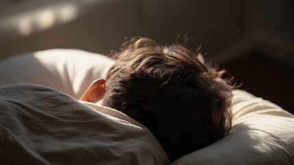 Close-up view of a human lying on a pillow with only the back of the head and shoulder visible in soft morning window light, symbolizing depression, mental stillness, and emotional hesitation to rise