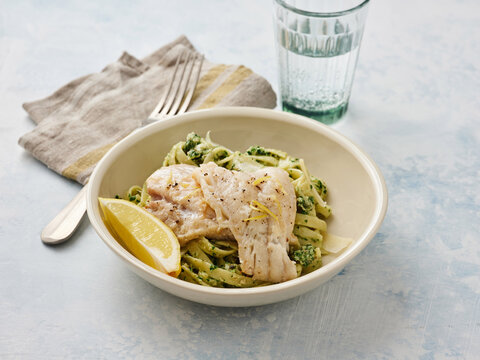 Prepared dish featuring lemon garlic pasta, succulent herb cod, and a slice of lemon, set against a soft blue background, ideal for sharing a meal at home