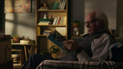 Side view shot of senior Caucasian man reading book sitting in armchair in his retro study - Powered by Adobe