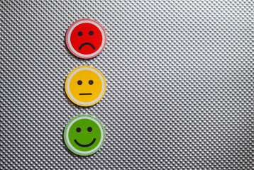 Three round emoji faces in red, yellow, and green representing sad, neutral, and happy emotions on a metallic textured background, symbolizing feedback or mood scale.