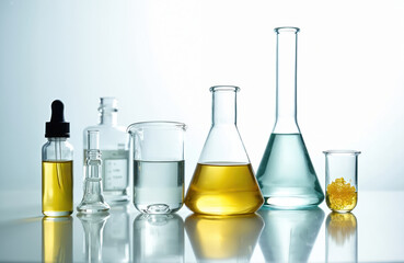 Variety of laboratory glassware with chemical liquids. Yellow cosmetic liquid in dropper bottle, clear fluid in beaker, yellow liquid in flask, solid crystals sample. Scientific research concept.