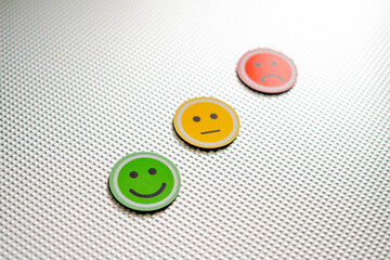 Three round emoji faces in red, yellow, and green representing sad, neutral, and happy emotions on a metallic textured background, symbolizing feedback or mood scale, selective focus in the green one