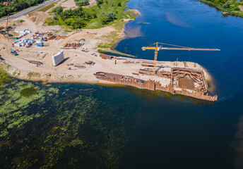 Construction site of new modern bridge construction in Kaunas, Lithuania. Aerial drone view of bridge connecting two shores of a river. Work progress