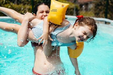 Older girl playing with younger girl in backyard pool