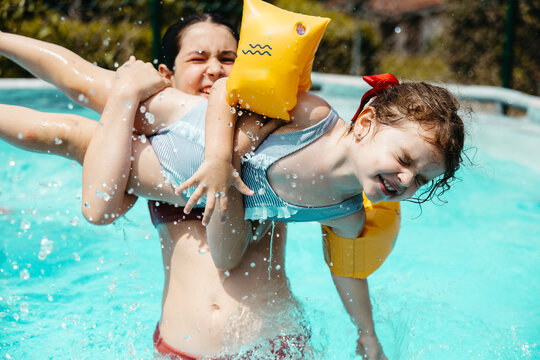 Older girl playing with younger girl in backyard pool