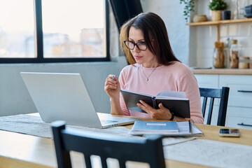 Middle-aged serious woman working at computer laptop in home office