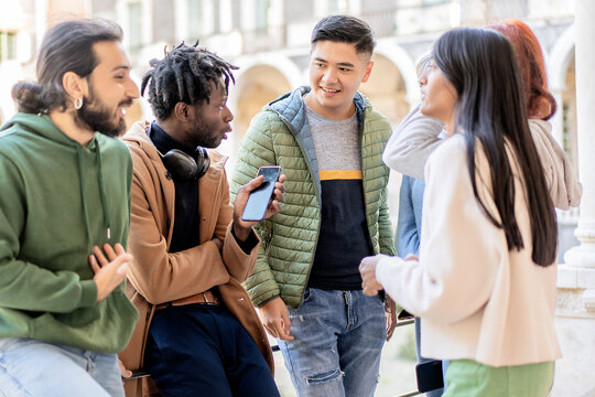 Multicultural group of young adults chatting and laughing together outdoors with smartphones in casual urban context