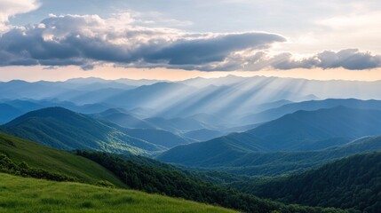 A scenic view of layered mountain ranges with sunlight piercing through the clouds above them