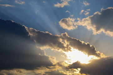 Dramatic sun rays breaking through clouds in the evening sky, creating a powerful atmosphere. The...