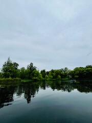 Grey cloudy sky reflection on the lake surface, silhouettes of the trees, lake surface as a mirror,...