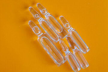Clear glass ampoules are evenly arranged on a vibrant orange background, creating a minimalist and...