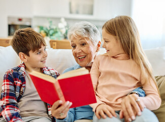 Portrait of grandmother with granddaughter and grandson grandchildren having fun together reading a...