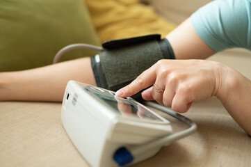 Close-up of European woman using digital blood pressure monitor. Finger pressing start button,...