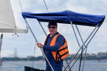 A 45-year-old man wearing sunglasses and a panama hat is at the helm of a yacht sailing on the sea.