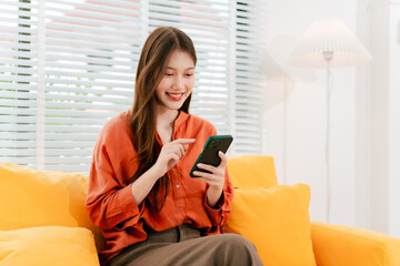 Beautiful Asian woman playing social media using smartphone at home. Woman is shopping and chatting with friends online.